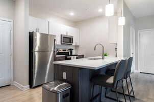 Una cocina moderna con electrodomésticos de acero inoxidable, una isla central con taburetes y lámparas colgantes.