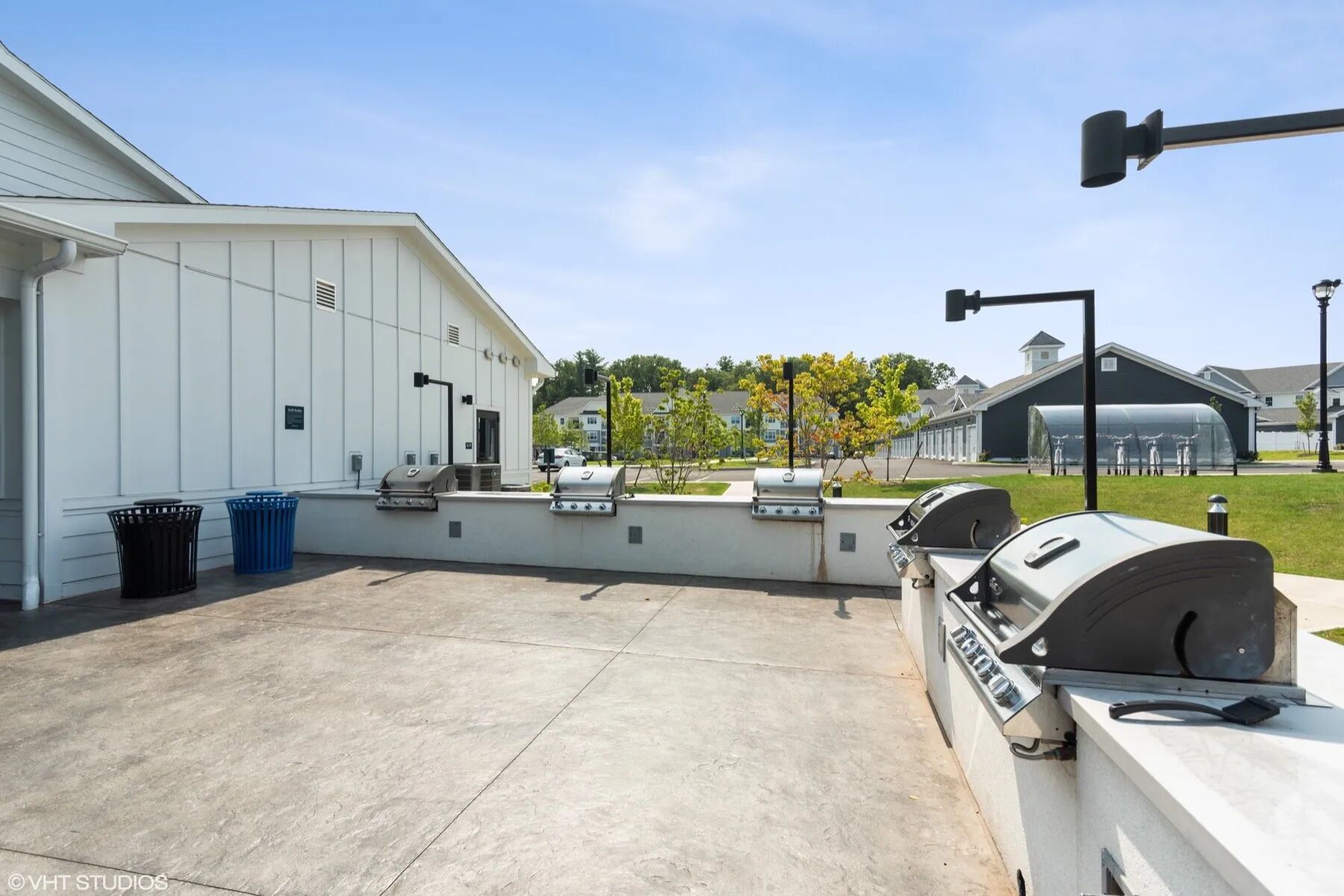 An outdoor patio with multiple barbecue grills, a concrete floor, and a white building in the background.
