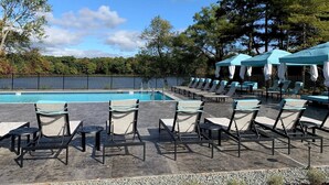 A poolside area with lounge chairs and umbrellas, surrounded by trees and a fence. - Landing Apartments West Windsor (Windsor)