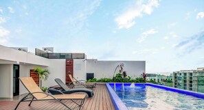 A rooftop pool area with lounge chairs, a wooden deck, and a clear blue sky. - Vibrant Condo by 5th Ave | Roof Pool | Gym | BBQ (Playa del Carmen)
