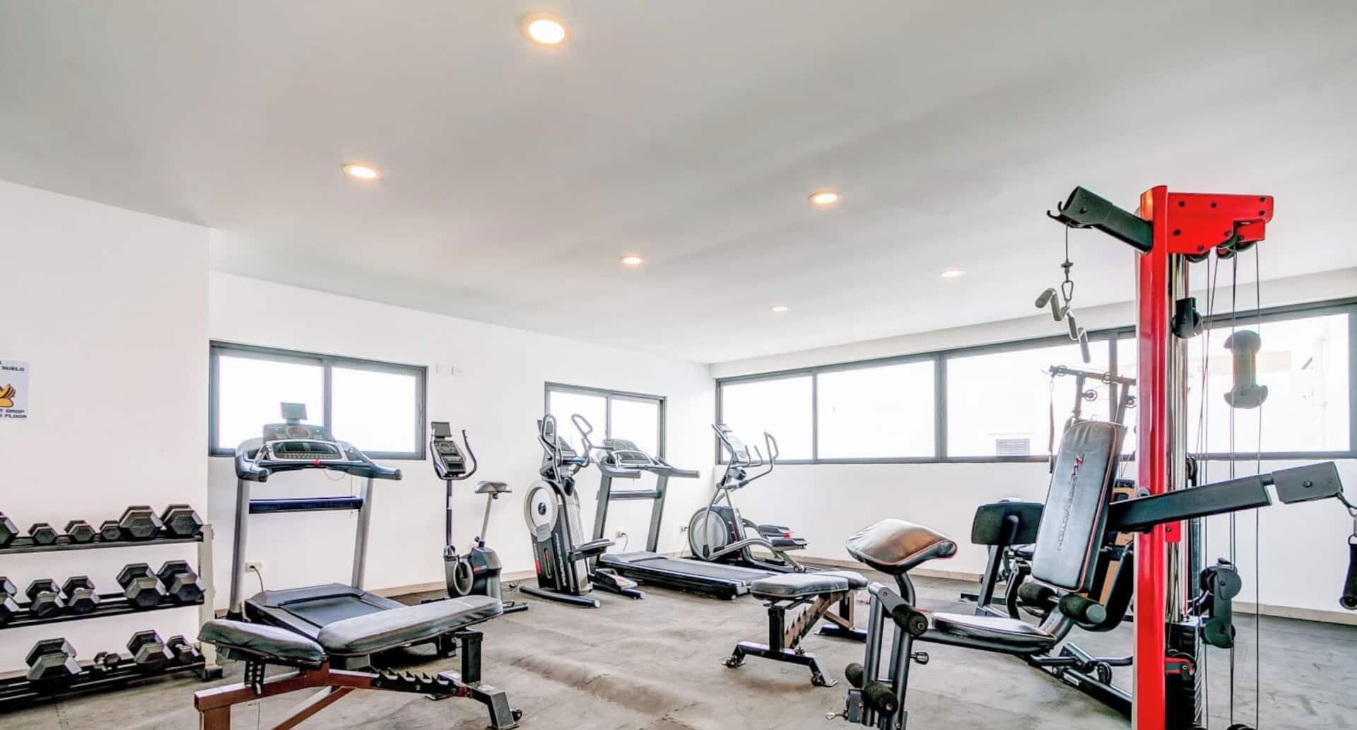 Ein Fitnessstudio mit unterschiedlichen Trainingsgeräten, darunter Laufbänder, Crosstrainer und Kurzhanteln.