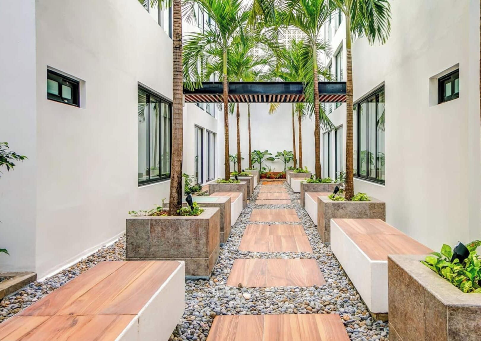 A corridor with a wooden floor, stone planters, and a row of palm trees.