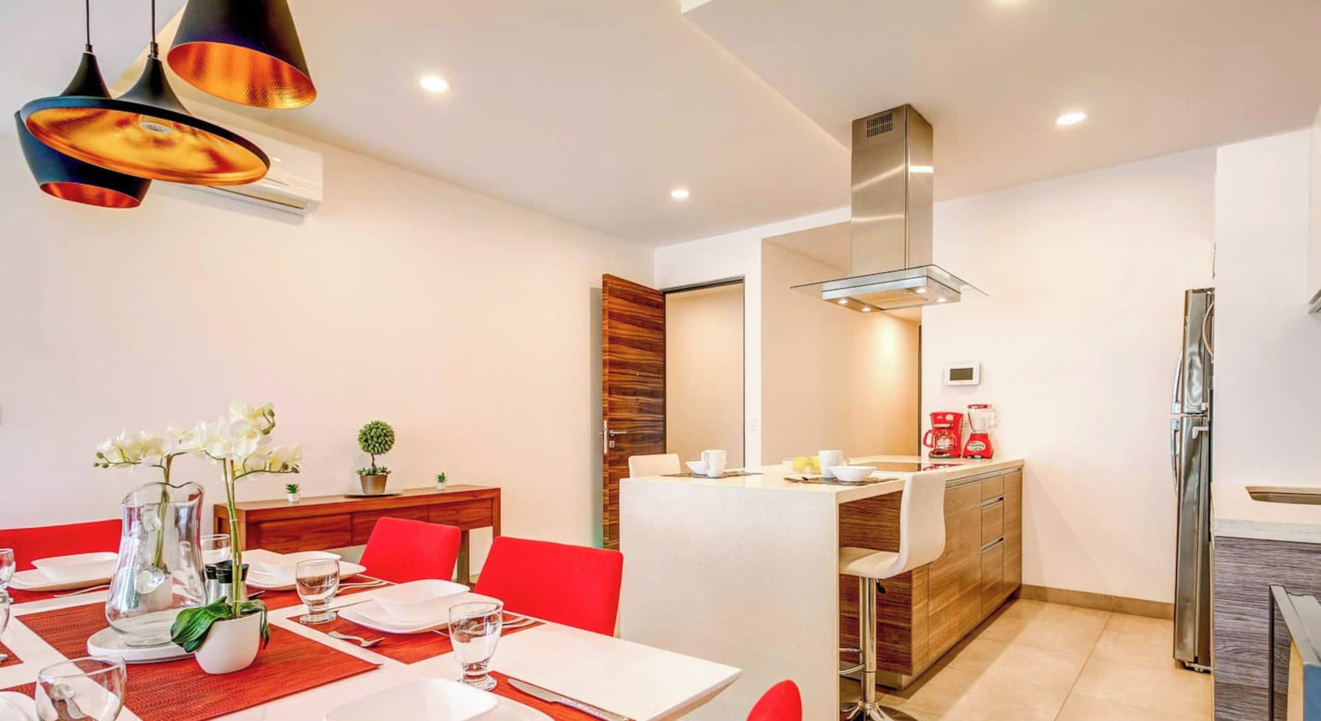 A modern dining area with a table set for two, a kitchen area with a refrigerator, and a built-in stove.