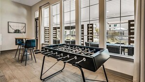 Una habitación con mesa de fútbol de mesa, ventanas amplias y vista al patio exterior.