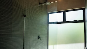 Ein modernes Badezimmer mit Duschkabine aus Glas, Toilette und großem Fenster für natürliches Licht.