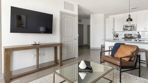 A modern living room with a glass coffee table, a brown leather chair, and a mounted flat-screen TV.