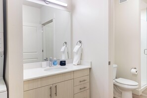 A modern bathroom with a white sink, mirror, and toilet. There are two towels hanging on the wall, a bottle of soap, and a makeup bag on the counter. - Landing Apartments Salt Lake City (Salt Lake City)