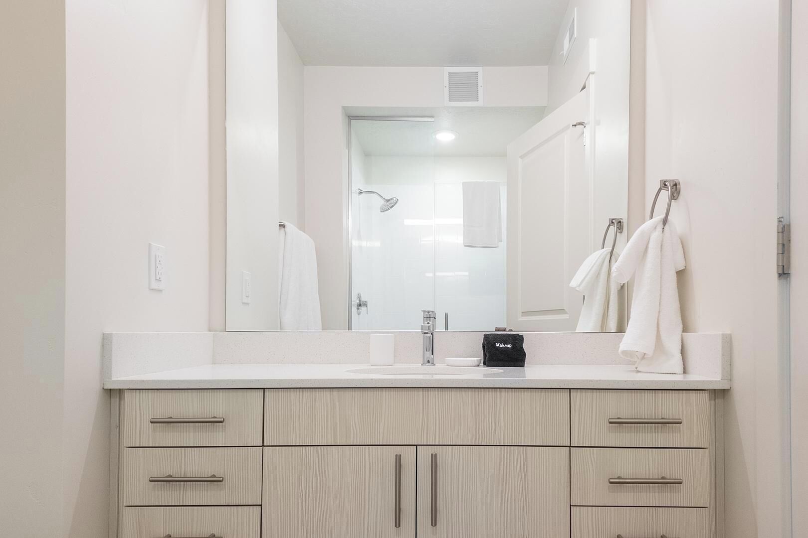 A modern bathroom with a large mirror, a sink, and a vanity with drawers.