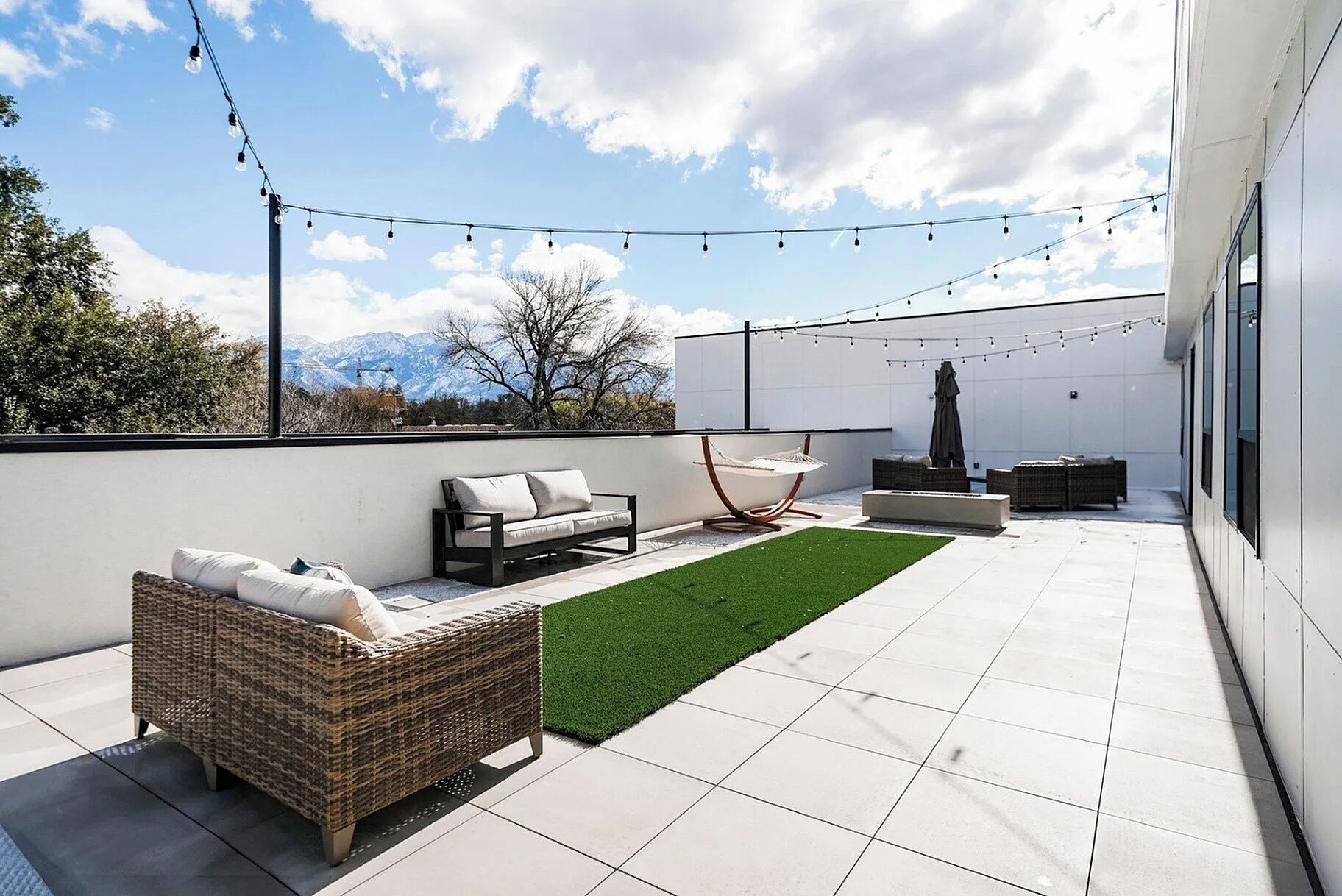 A rooftop patio with outdoor furniture, a hammock, and string lights.