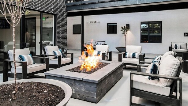 Area esterna con posti a sedere, un braciere, poltrone relax e un edificio moderno con un balcone.