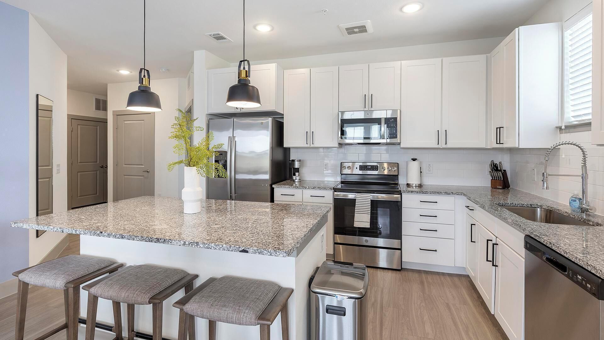 A modern kitchen with white cabinets, stainless steel appliances, granite countertops, and bar stools.