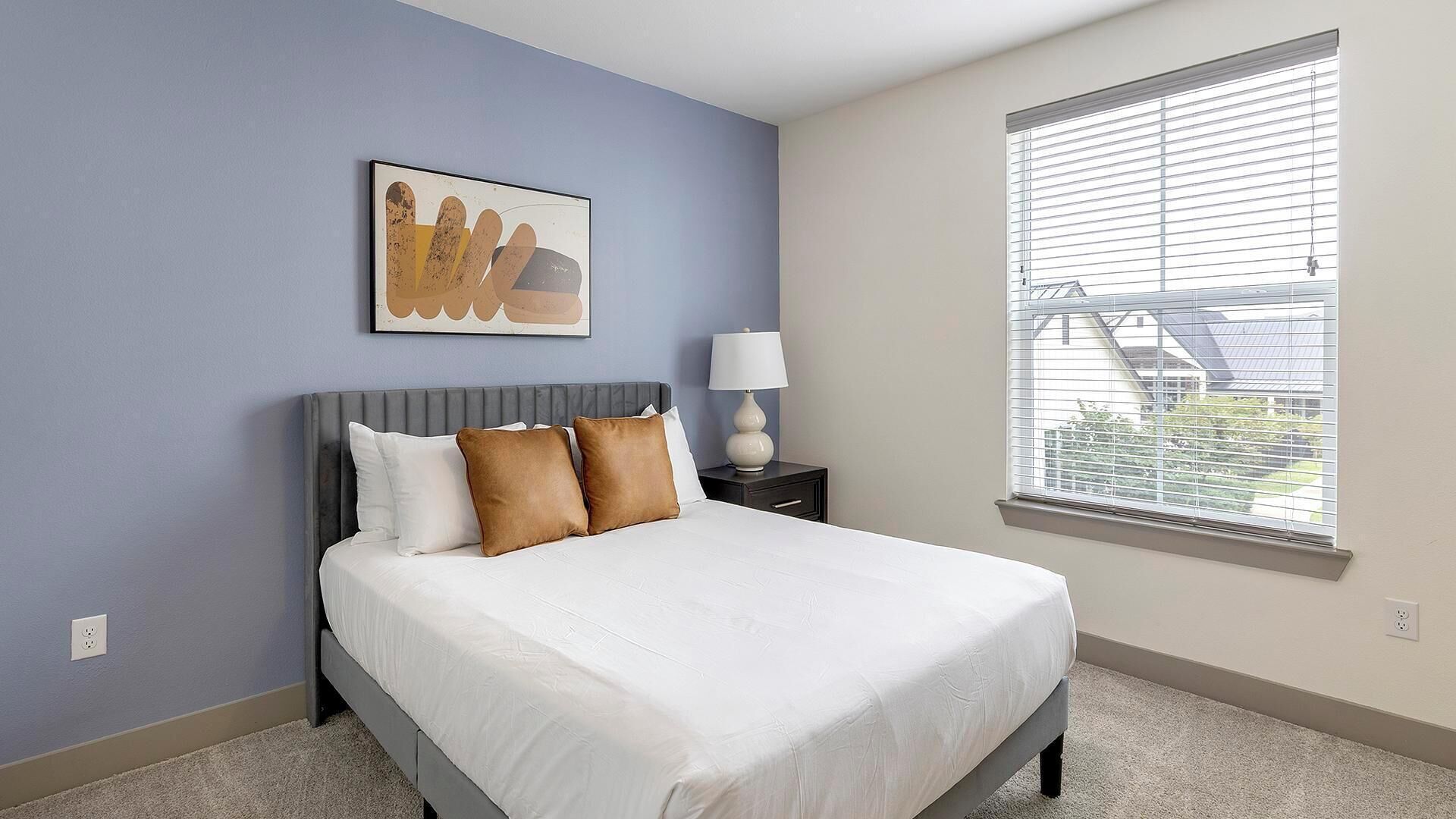 A bedroom with a bed, a nightstand, a lamp, and a window with blinds.