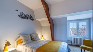 Ein Schlafzimmer mit Bett, Nachttisch, Lampe, Stuhl und einem Fenster mit Blick.