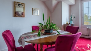 Ein Essbereich mit einem runden Holztisch, roten Samtstühlen, einem Blumentopf, einem Spiegel und einem gerahmten Bild an der Wand.