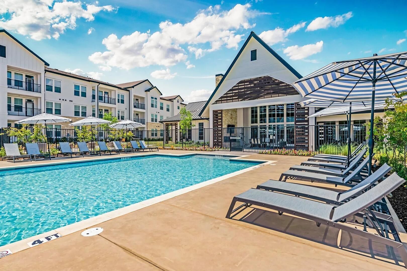 A swimming pool with lounge chairs and umbrellas, surrounded by apartment buildings.