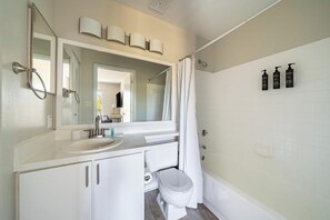 Ein Badezimmer mit weißem Waschbecken, Spiegel und Toilette, einer Duschvorhang und drei Pflegeprodukten an der Wand.
