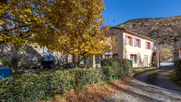 Un edificio in pietra con un muro di pietra, un vialetto lastricato e un albero con foglie gialle.