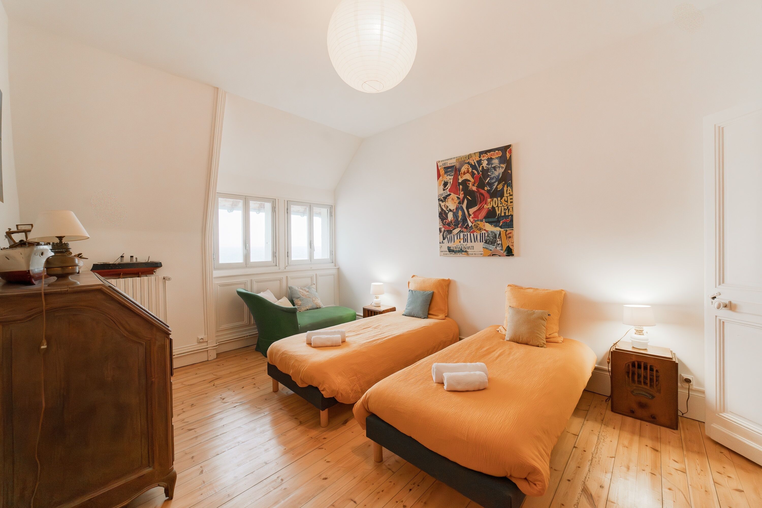 Una habitación con dos camas, una silla verde, un armario de madera y un cartel en la pared.