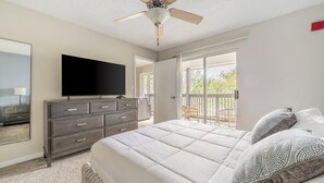 Une chambre à coucher comprenant un lit, une commode, un téléviseur et un ventilateur de plafond.