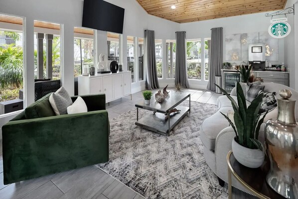 A modern living room with a green sofa, a coffee table, and a TV mounted on the wall. - Landing | Incredible 2BD, Gym, Tennis Court (Palm Bay)