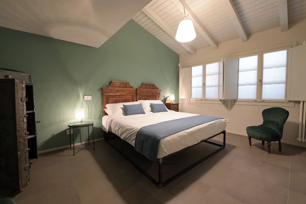 Une chambre à coucher avec un lit, une chaise, une commode et une fenêtre avec des stores.