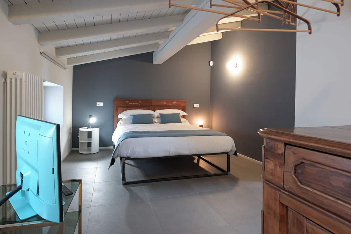 Une chambre à coucher moderne avec un lit, des lampes de chevet, une commode en bois et une table en verre sur laquelle se trouve un écran d’ordinateur.