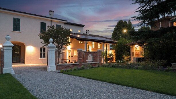 A well-lit building with a gravel driveway and a grassy area. - Villa Bredina (Brescia)