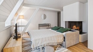Une chambre de style loft moderne, avec un plafond en pente, une cheminée, un lit agrémenté de coussins verts et un petit bureau avec une lampe.
