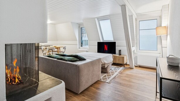 Une chambre de style loft moderne, dotée d’une cheminée, d’un lit, d’un bureau et d’un téléviseur affichant le logo de Netflix.