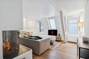 Een moderne loft slaapkamer met een open haard, een bed, een bureau en een televisie waarop het Netflix logo te zien is.