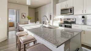 A modern kitchen with white cabinets, a granite countertop, a stainless steel sink, and a built-in oven. - Landing | Chic 2BD, Gym, Yoga Studio (Houston)