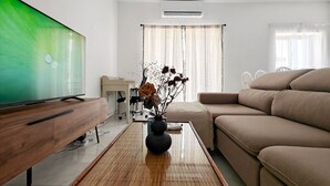 Ein modernes Wohnzimmer mit Flachbildfernseher, einer Couch, einem Couchtisch mit einer Vase und einem Schreibtisch mit Stuhl.