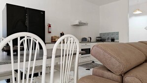 Ein modernes Wohnzimmer mit einer Couch, weißen Stühlen, einem schwarzen Fernseher und einer Küchenzeile mit Herd und Mikrowelle.