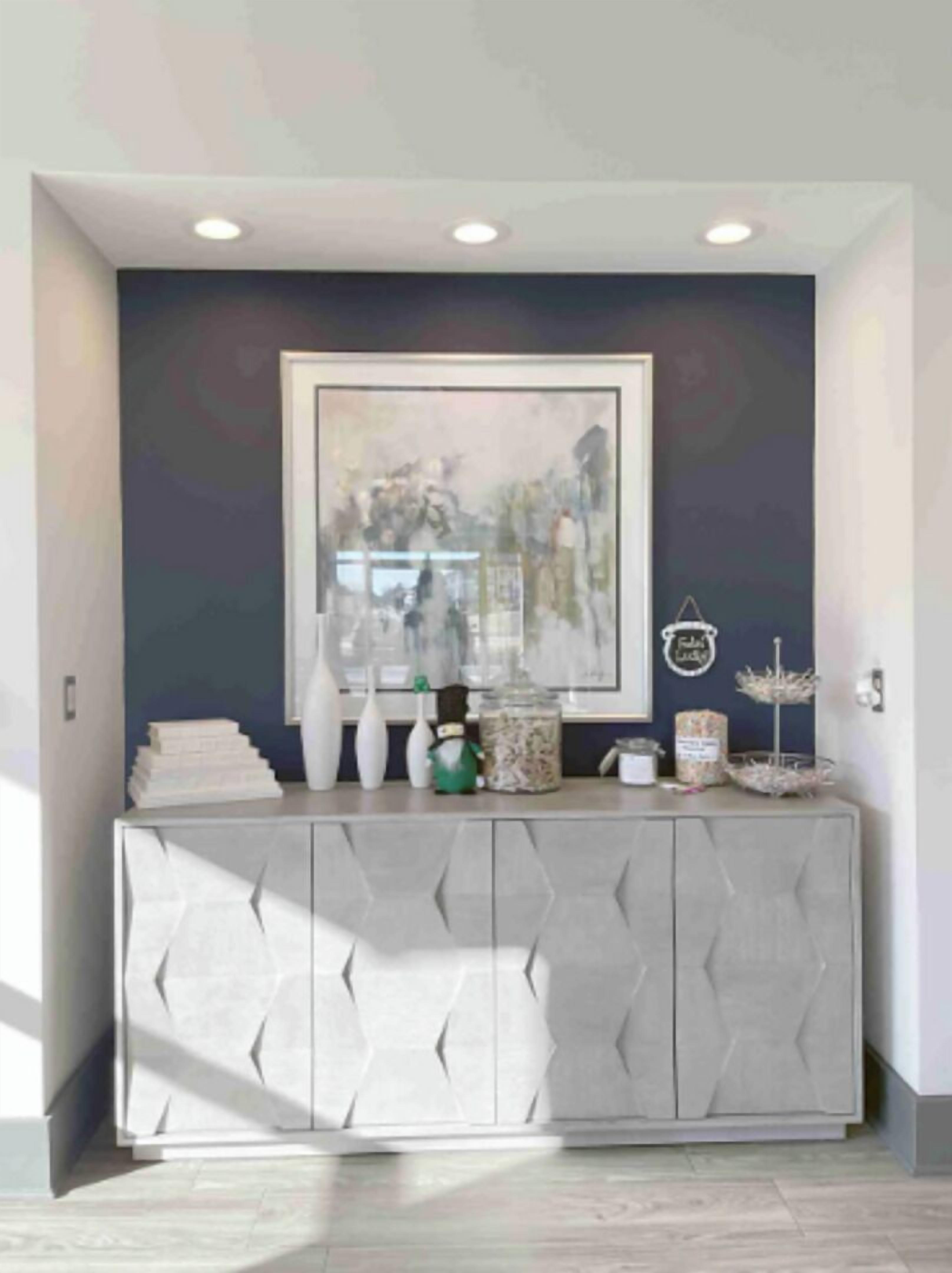 A modern living room with a dark blue accent wall, a framed abstract painting, and a geometric-patterned cabinet with decorative items.