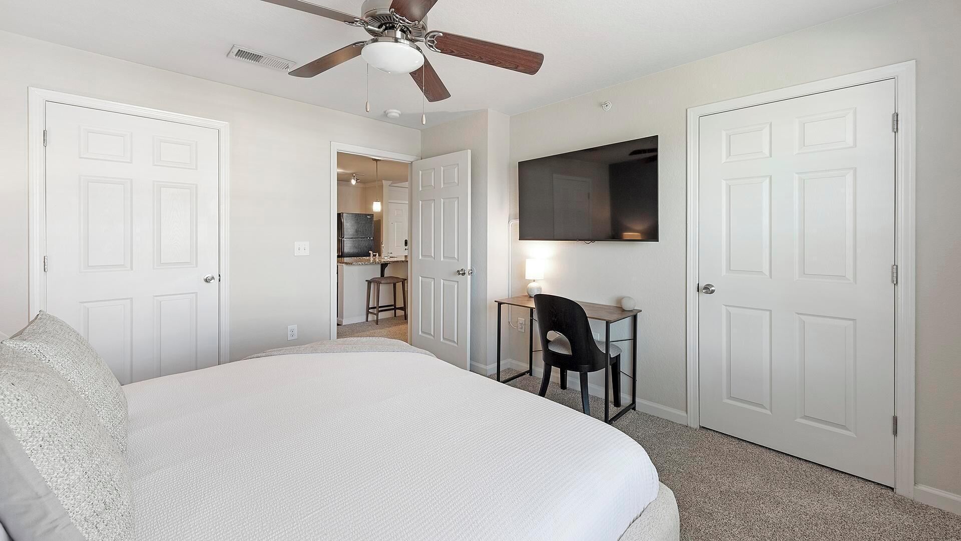 Quarto com cama, escrivaninha, cadeira e ventilador de teto.