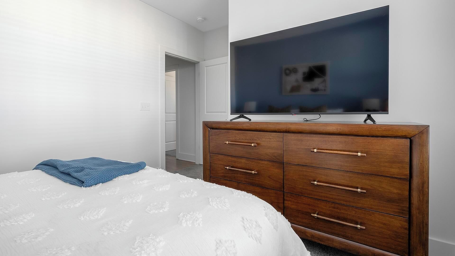 A bedroom with a bed, a dresser, and a television mounted on the wall.
