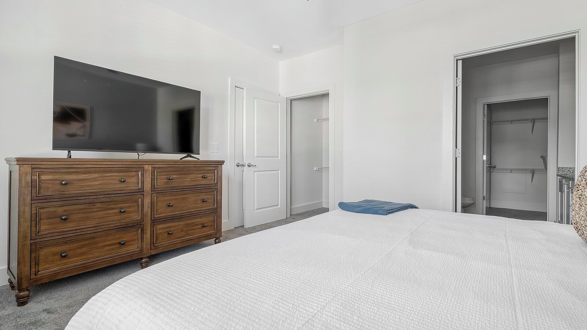 Une chambre à coucher avec un grand lit, une commode en bois, un téléviseur à écran plat et un dressing.