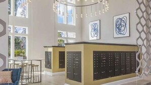 Un hall d’hôtel spacieux, doté d’un comptoir d’accueil central, d’un éclairage moderne suspendu et de grandes fenêtres laissant entrer la lumière naturelle.