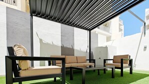 Een terras met een pergola, een bank, een stoel en een tafel, gelegen op kunstgras.