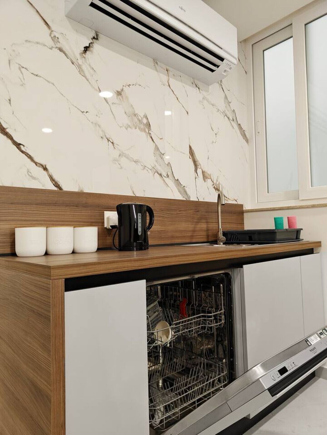 Una cocina moderna con protector contra salpicaduras de mármol, lavavajillas integrado y cafetera sobre la encimera.