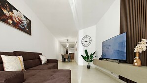 Een moderne woonkamer met een hoekbank, een flatscreen televisie, een klok aan de muur en een potplant.