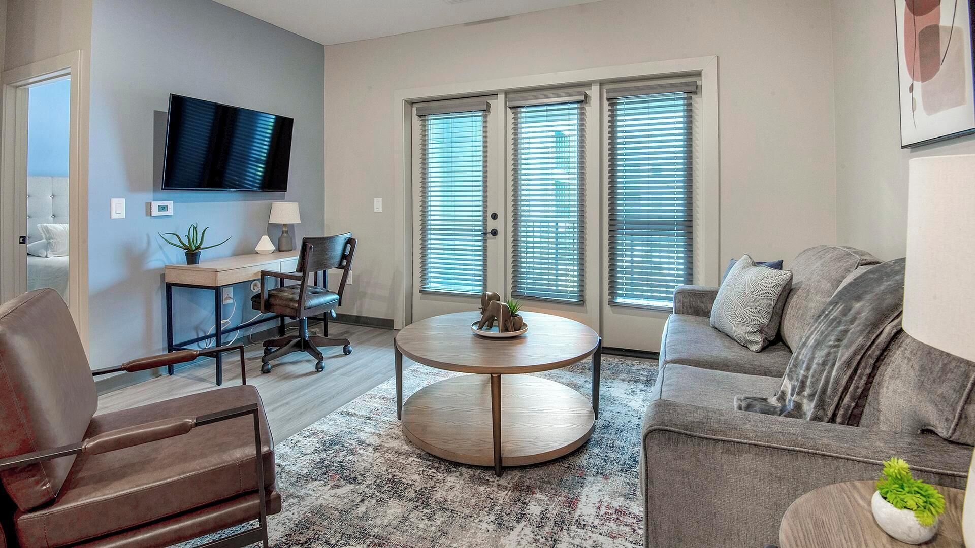 A modern living room with a round coffee table, a sofa, a desk with a chair, and a TV mounted on the wall.