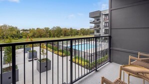 A balcony with a view of a swimming pool, outdoor seating, and a landscaped area.