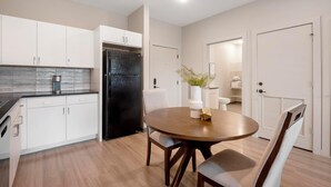 A modern kitchen with white cabinets, a black refrigerator, and a dining area with a wooden table and chairs.