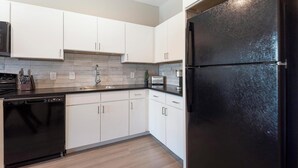 A modern kitchen with white cabinets, a black refrigerator, a dishwasher, and a microwave. - Landing | Incredible 1BD, Rooftop Lounge, Pool (Memphis)