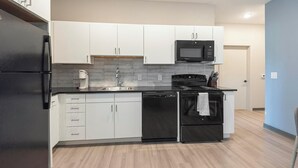 Una cocina moderna con armarios blancos, un refrigerador negro, un microondas, un lavavajillas y una estufa.