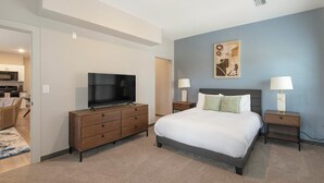 Un dormitorio con una cama, un televisor sobre un tocador, dos mesitas de noche con lámparas y un cuadro en la pared.