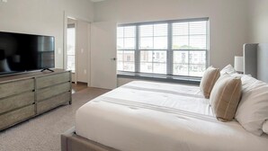 Un dormitorio con una cama grande, un televisor sobre un aparador y una ventana con persianas.