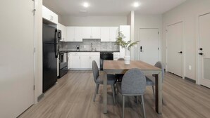 Una cocina moderna con armarios blancos, un refrigerador negro, una mesa de comedor de madera con cuatro sillas y una planta en maceta.