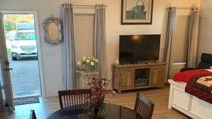 A dining area with a round table, chairs, a vase with flowers, a television on a stand, and a bed with a red blanket. - Fully Furnished Studio Directly Across from TMH (Tallahassee)